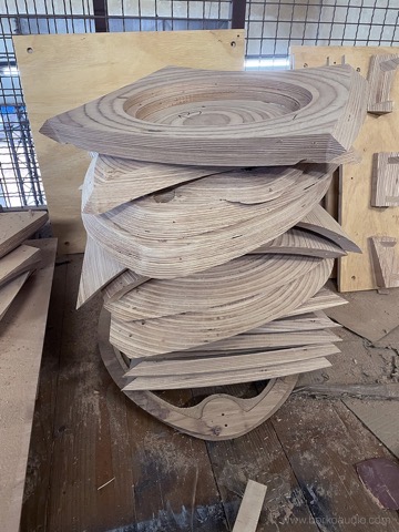 CNC-cut plywood cabinet layers stacked on a pallet in the Borko Audio workshop